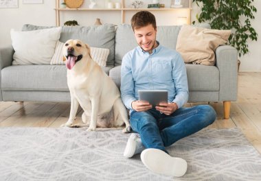 Evde tabletli ve köpekli genç bir adam var.