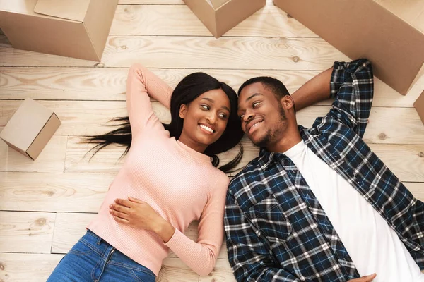 Smiling African American couple with cardboard boxes having rest on moving day, top view