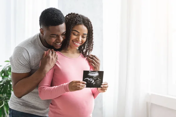 Souriant couple noir enceinte montrant l'image échographique de leur bébé — Photo