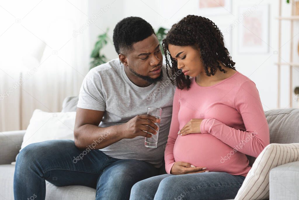 Black pregnant woman feeling sick, husband giving glass of water
