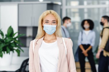 Modern yönetici karantinadan sonra işe geri döner. Koruyucu maske ve takım elbiseli çekici sarışın kadına odaklanın. Bulanık geçmişi olan çalışanlara.