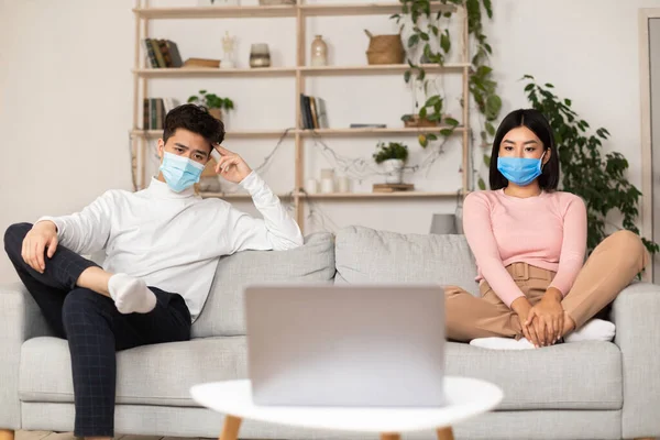 Азиатская пара в масках, смотрящая кино во время самоизоляции дома — стоковое фото