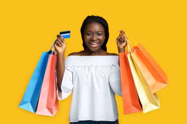 Büyük alışveriş. Neşeli siyah kadın alışveriş torbaları ve kredi kartıyla poz veriyor