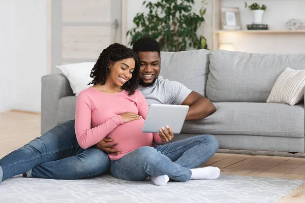 Pregnant black couple having fun at home, using digital tablet — Stock Photo, Image