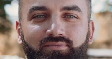 Kameraya göz kırpan sakallı adamın portresi, bulanık sonbahar parkı arka planı