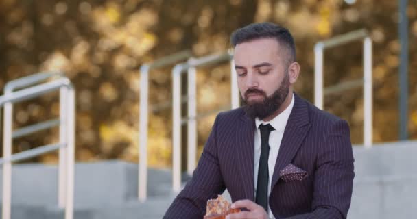Biznesmen w średnim wieku je pizzę w jesiennym parku, odpoczywając od biura — Wideo stockowe