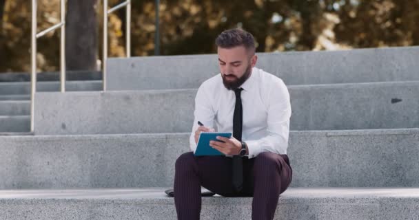 Homem de negócios concentrado criando plano de marketing, sentado em escadas no parque — Vídeo de Stock