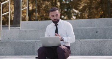 Mutlu orta yaşlı işadamı sonbahar parkında dizüstü bilgisayarda çalışıyor ve merdivenlerde dans ediyor.