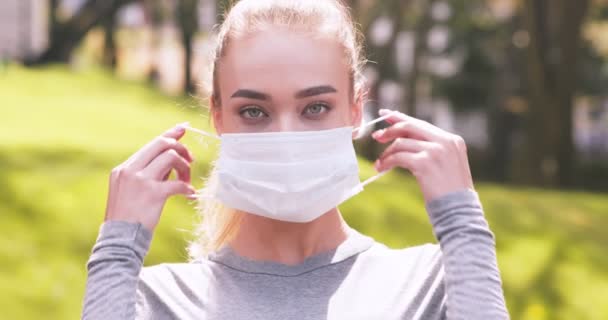 Novo conceito normal. Retrato ao ar livre de jovem mulher loira colocando máscara protetora — Vídeo de Stock