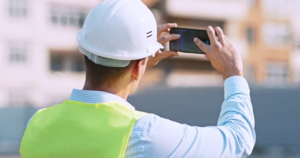 Werknemer op de bouwplaats maakt foto 's op zijn mobiele telefoon, achteraanzicht, tracking shot — Stockvideo