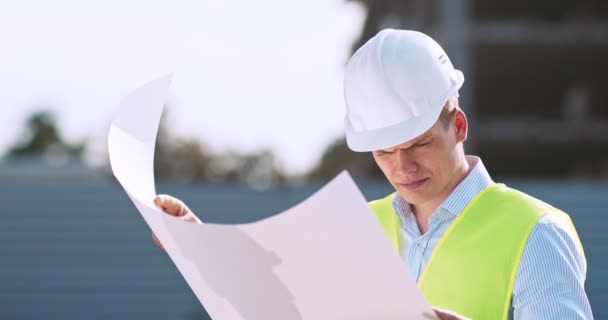 Инженер-строитель мужчина рабочий архитектор в защитном шлеме изучает чертеж плана на строительной площадке — стоковое видео