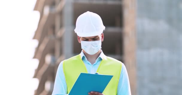 Man architect in beschermende masker inspecteren gebouw, het controleren van onroerend goed plan op de bouwplaats — Stockvideo