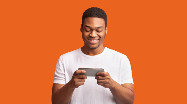 Érdeklődő afro srác használ okostelefon felett narancs háttér — Stock Fotó