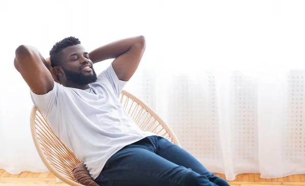 Mladý Afričan relaxuje doma, odpočívá na židli — Stock fotografie