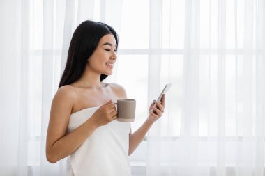 Güzel Asyalı kadın akıllı telefon kullanıyor ve kahve içiyor.