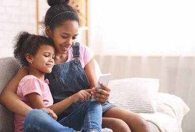 Küçük Afrikalı Amerikalı kız, kız kardeşinin cep telefonuyla oynuyor.