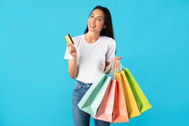 Kredi kartı tutan ve alışveriş torbaları taşıyan bir kadın.