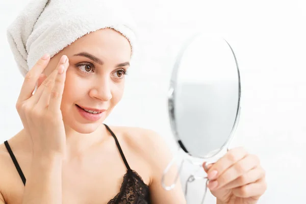 Tysiąclecia kobieta masuje twarz, patrząc w lustro — Zdjęcie stockowe