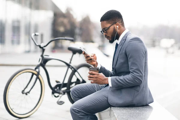 Μαύρος επιχειρηματίας με ακουστικά που στέλνει μηνύματα στο τηλέφωνο πίνοντας τσάι — Φωτογραφία Αρχείου