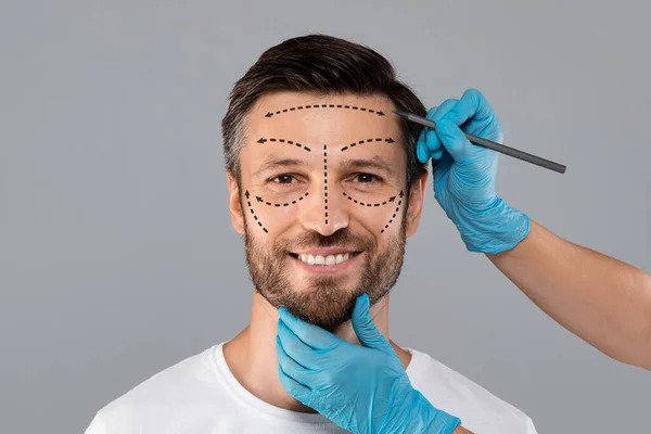 Surgeon hands making marks on smiling man face