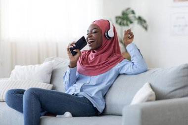 Mobil Karaoke. Neşeli Siyah Müslüman Kadın Evde Akıllı Telefonla Şarkı Söylüyor