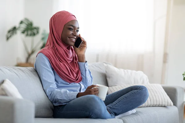Lazító hétvége. Vidám fekete muszlim nő beszél mobilon és élvezi a kávét — Stock Fotó