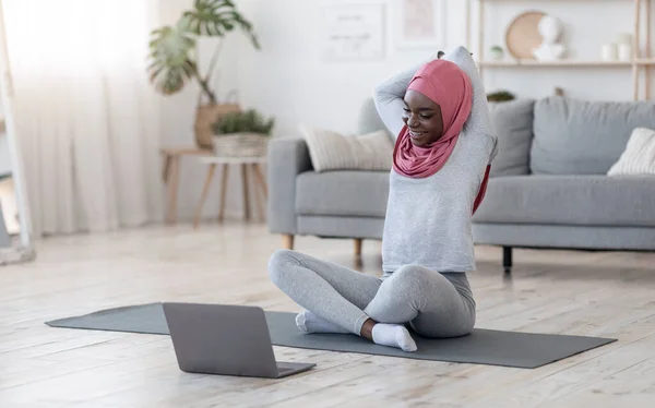 Тренировка дома. Fit черный мусульманин женщина делает упражнения на растяжку с ноутбуком — стоковое фото