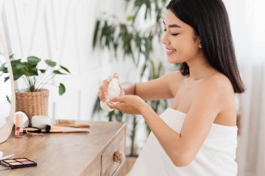 Neşeli Asyalı kadın tonerle yüzünü temizliyor.