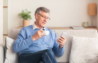 Son sınıf öğrencisi akıllı telefon kullanıyor. Oturduğu koltukta kahve içiyor.