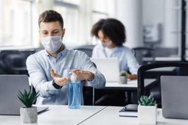 Coronavirüs salgını sırasında güvenlik kuralları. Koruyucu maskeli bir adam iş yerinde ellerini antiseptikle tedavi ediyor.