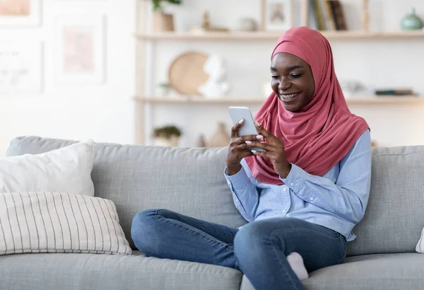 Közösségi hálózatok. Fiatal fekete muszlim nő hidzsáb segítségével okostelefon otthon — Stock Fotó