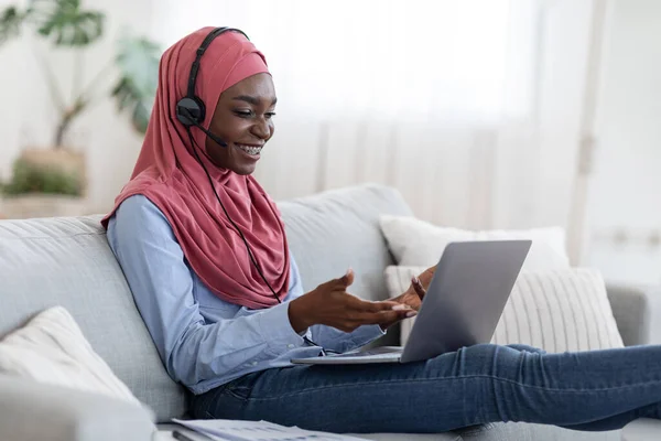 Online üzleti találkozó. Fekete muszlim hölgy használ headset és laptop otthon — Stock Fotó