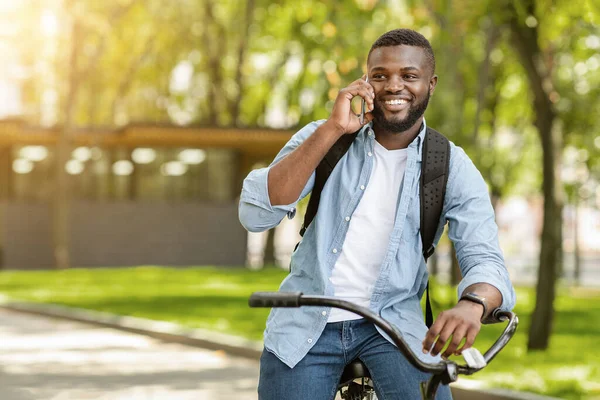 Sorrindo preto cara falando no celular enquanto andar de bicicleta ao ar livre — Fotografia de Stock