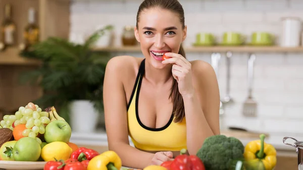 Sportowa kobieta gryzie pomidory wiśniowe w domu kuchnia — Zdjęcie stockowe
