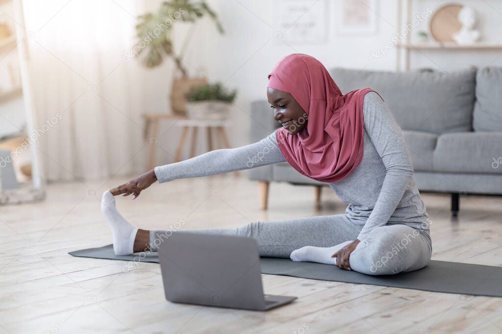 Home Training. Sporty black muslim woman stretching in front of laptop