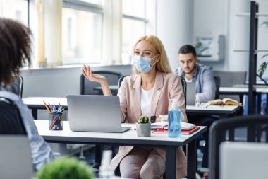 Yönetici ve müvekkil ile istişare. Koruyucu maskeli genç bir iş kadını Afrikalı Amerikalı bir bayanla konuşuyor.