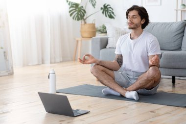 Lotus pozisyonunda oturan konsantre genç adam.