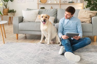 Tablet ve köpekle oturan genç adam.