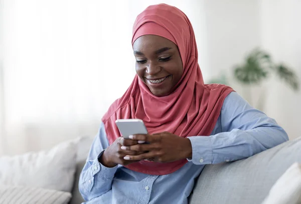 Προσφορά κινητού. Χαρούμενη μαύρη μουσουλμάνα κυρία Μηνύματα στο Smartphone στο σπίτι — Φωτογραφία Αρχείου