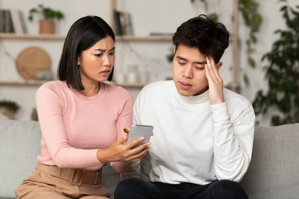 Chinês namorada mostrando batota namorado seu celular sentado em casa — Fotografia de Stock