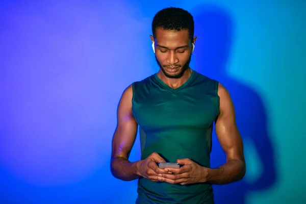 Deportivo hombre negro usando teléfono y auriculares en fondo azul —  Fotos de Stock