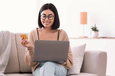 Genç bir kadın yerde oturmuş alışveriş yapıyor.