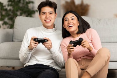 Çinli çift içeride koltukta oturmuş video oyunu oynuyor.
