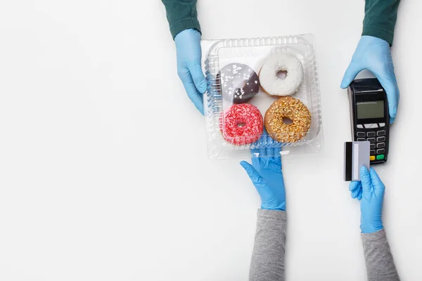 Sweets and cake set and modern payment. Client picks up container of donuts with bright glaze and pay by credit card at terminal — Stock Photo, Image