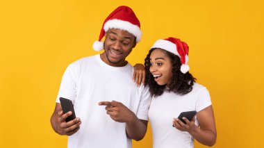 Siyah Çift Cep Telefonu Tutuyor. Sarı Arkaplan Üzerinde Noel Uygulaması Tavsiye Ediyor