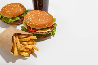 Restoran menüsünde fast food seti ve modern öğle yemeği. Hamburger ve çizburger, patates kızartması kağıt ambalajda ve kola bardakta.