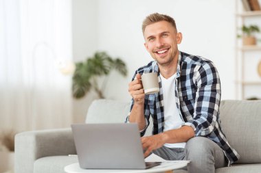 Mutlu yakışıklı adam kanepede oturup kahve içiyor.