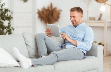 Dijital tablet kullanan mutlu adam koltukta oturuyor.