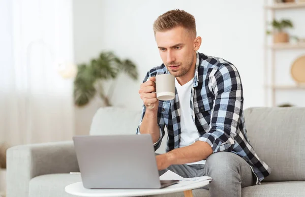 Retrato de homem sentado no sofá com café usando pc — Fotografia de Stock