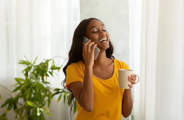 Charmig svart kvinna talar på mobiltelefon med kopp aromatiskt kaffe hemma — Stockfoto